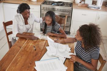 Mother Helping Two Daughters Sitting At Table Doing Homework