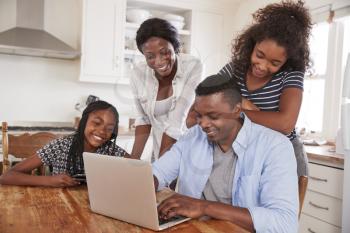 Family Around Kitchen Table Booking Vacation On Laptop Together