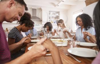 Two Families Saying Grace Before Eating Meal Together