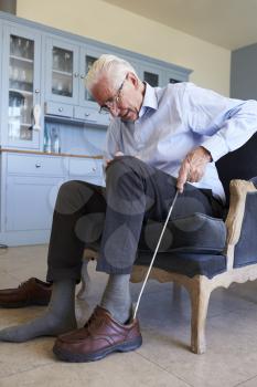 Senior Man In Chair Using Aid To Put On Shoe