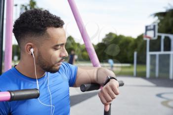 Young man at outdoor gym checking fitness app on smartwatch