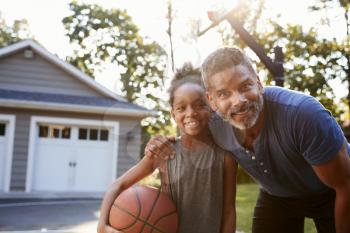 Portrait Of Father And Son Playing Basketball On Driveway