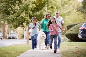 Grandparents And Granddaughters Walking Dog Along Street