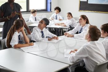 Detail Of Female High School Tutor Helping Students Wearing Uniform Seated Around Tables In Lesson