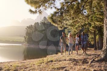Group Of Young Friends Enjoying Walk By Lake On Hiking Adventure