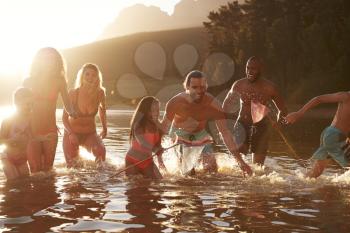 Family With Friends Enjoying Evening Swim In Countryside Lake