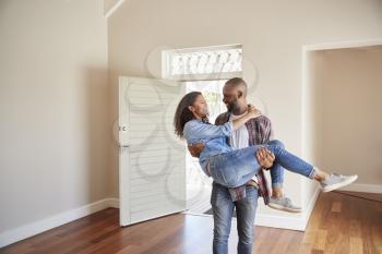 Man Carrying Woman Over Threshold Of Doorway In New Home