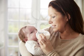 Mother Feeding Newborn Baby From Bottle At Home