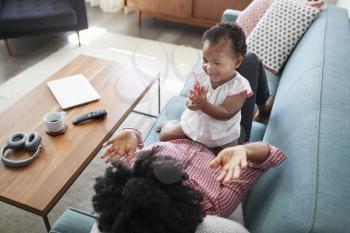 Mother Lying On Sofa At Home Playing Clapping Game With Baby Daughter