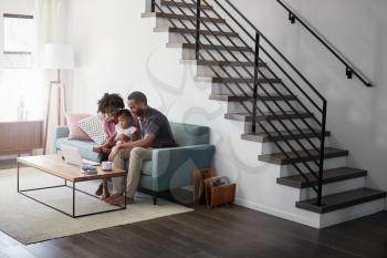 Family With Baby Daughter Sitting On Sofa At Home Looking At Laptop Computer