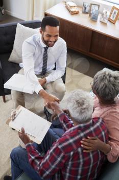 Senior Couple Shaking Hands With Male Financial Advisor At Home