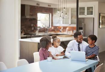 Parents Sitting Around Table At Home Helping Children With Homework