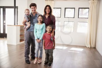Portrait Of Happy Family With Baby Standing In Empty Lounge Of New Home