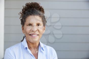 Portrait Of Senior Woman Standing Outside Grey Clapboard House