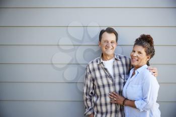 Portrait Of Senior Couple Standing Outside Grey Clapboard House