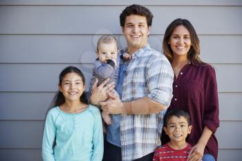 Portrait Of Happy Family With Baby Standing Outside Grey Clapboard House