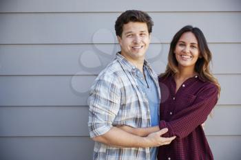 Portrait Of Couple Standing Outside Grey Clapboard House