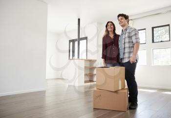 Excited Couple Standing With Boxes In New Home On Moving Day