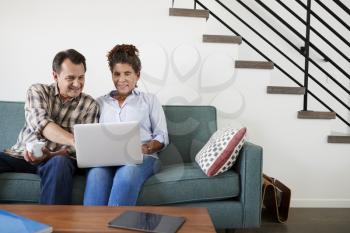 Senior Couple Sitting On Sofa At Home Using Laptop Together