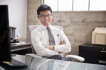 Young Asian businessman at an office desk, smiling to camera