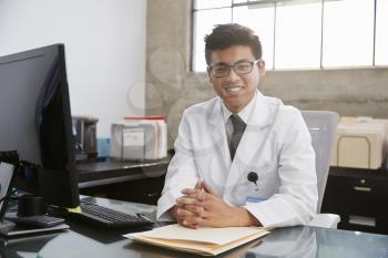 Young Asian male doctor sitting at desk, portrait