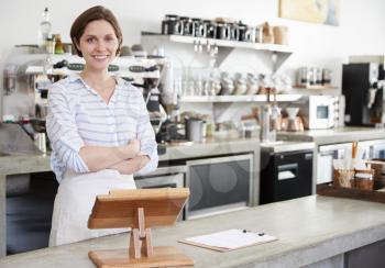 Smiling woman behind counter at a coffee shop, arms crossed