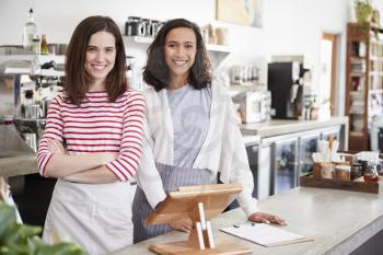 Two female coffee shop owners smiling behind the counter