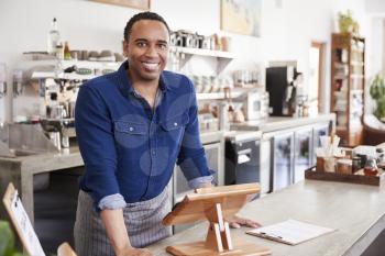 Young black male coffee shop owner leaning behind counter