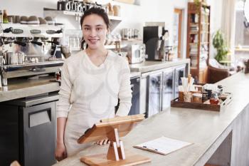 Female coffee shop owner standing behind counter smiling