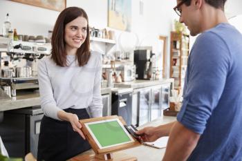 Male customer makes contactless card payment at coffee shop