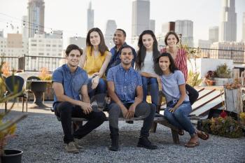 Portrait Of Friends Gathered On Rooftop Terrace For Party With City Skyline In Background