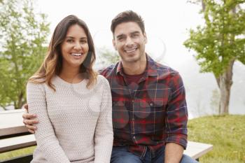 Young smiling couple sit embracing in a park