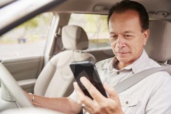 Senior man in car checking his smartphone while driving