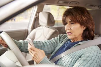 Senior woman in car checking her smartphone while driving