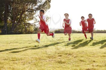Four young boys in football strip running in a playing field