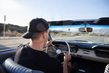 Rear View Of Man On Road Trip Driving Classic Convertible Car Towards Sunset