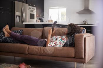 Woman Lying On Sofa At Home Using Digital Tablet