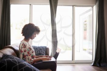 Side View Of Woman Sitting On Sofa At Home Using Laptop