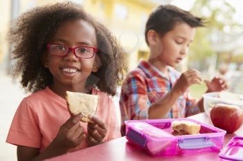 Young school girl and boy with packed lunches look to camera