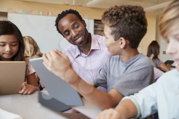 Teacher using tablet computer at desk with school kids