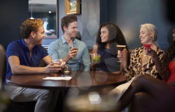 Group Of Young Friends Sitting Around Table In Bar Together On Night Out