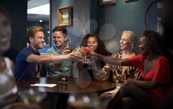 Group Of Young Friends Sitting Around Table And Making A Toast In Bar On Night Out