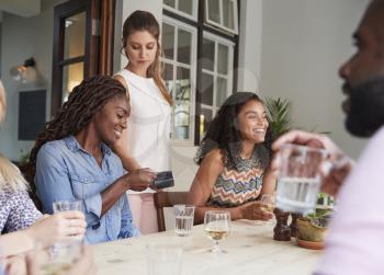 Female Customer In Restaurant Paying Bill Using Contactless Credit Card Terminal