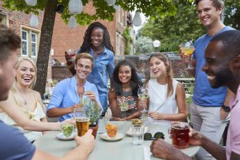 Friends Sitting At Table In Pub Garden Enjoying Drink Together