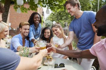 Friends Sitting At Table In Pub Garden Making Toast Together