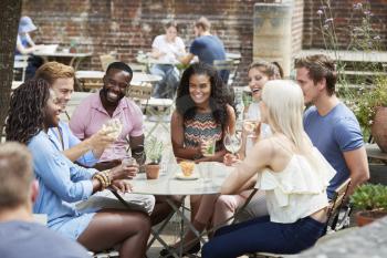 Friends Sitting At Table In Pub Garden Enjoying Drink Together