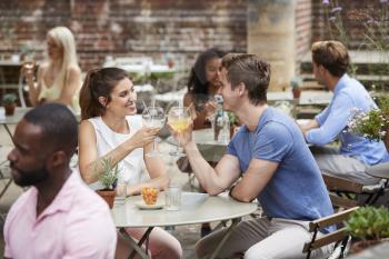 Couple Sitting At Table In Pub Garden Enjoying Drink Together