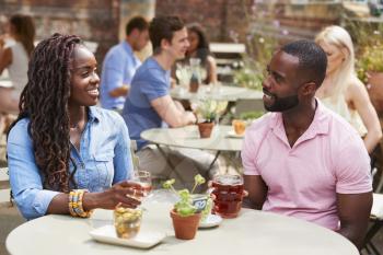Couple Sitting At Table In Pub Garden Enjoying Drink Together