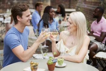Couple Sitting At Table In Pub Garden Making A Toast Together