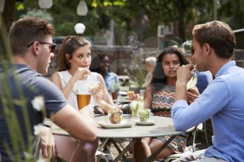 Friends Sitting At Table In Pub Garden Enjoying Drinks Together